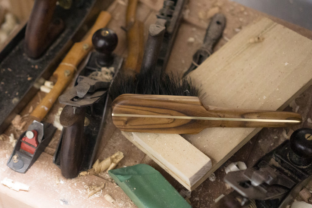 An olivewood and boarhair brush sitting amongst tools in a woodshop